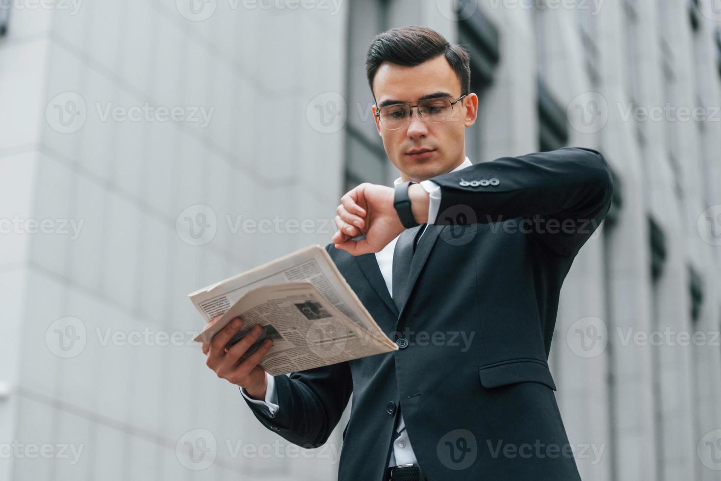 sosteniendo el periódico. hombre de negocios con traje negro y corbata está al aire libre en la ciudad foto