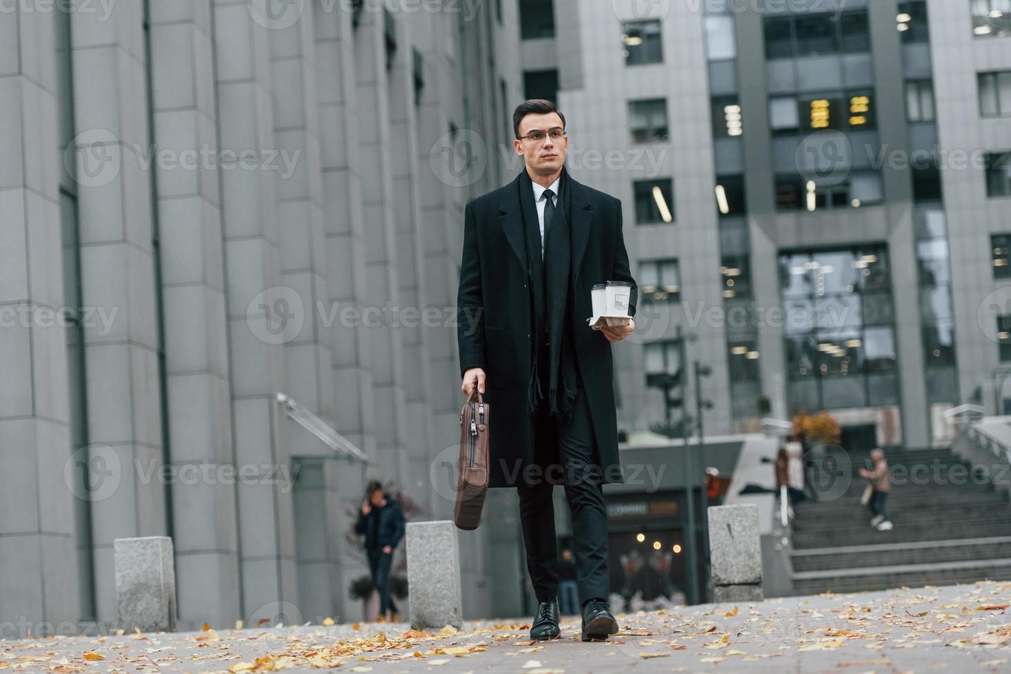 caminando hacia adelante hombre de negocios con traje negro y corbata está al aire libre en la ciudad foto