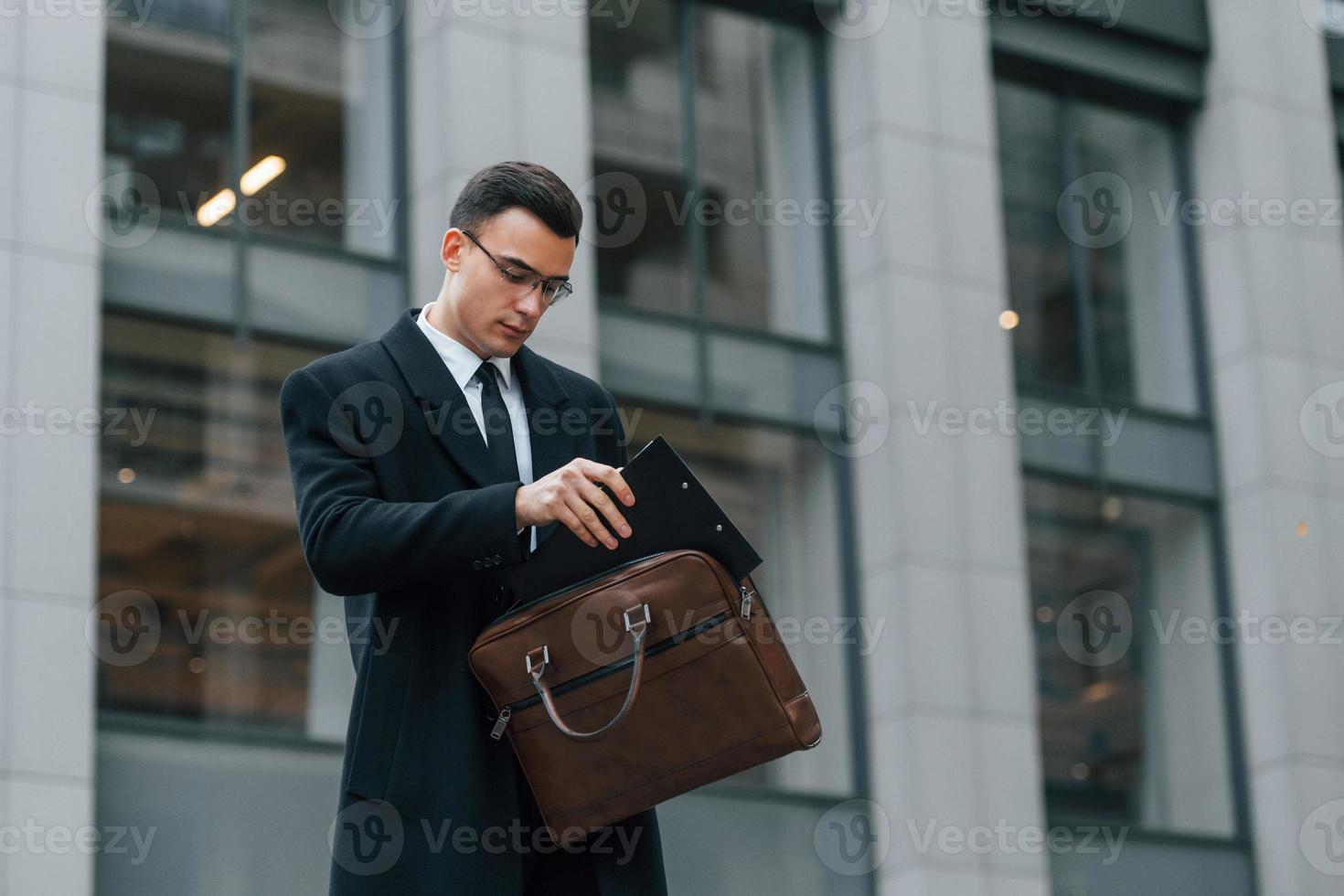 With brown bag. Businessman in black suit and tie is outdoors in the city photo