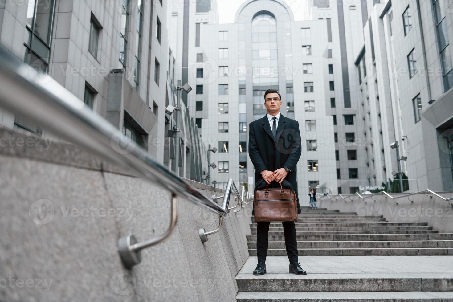 Buildings exterior. Businessman in black suit and tie is outdoors in the city photo