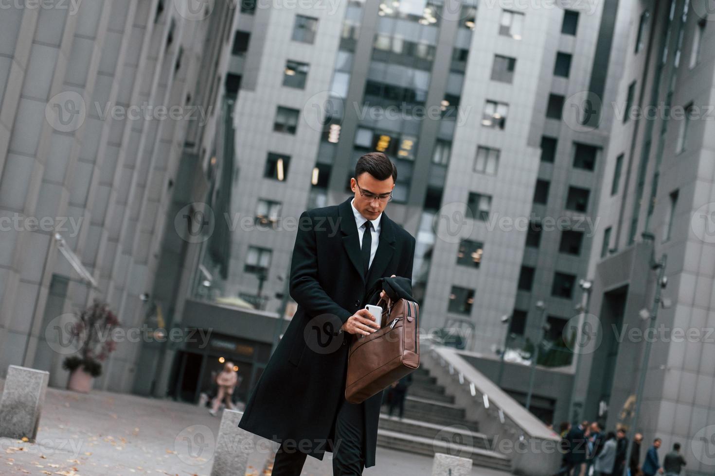 In formal clothes. Businessman in black suit and tie is outdoors in the city photo