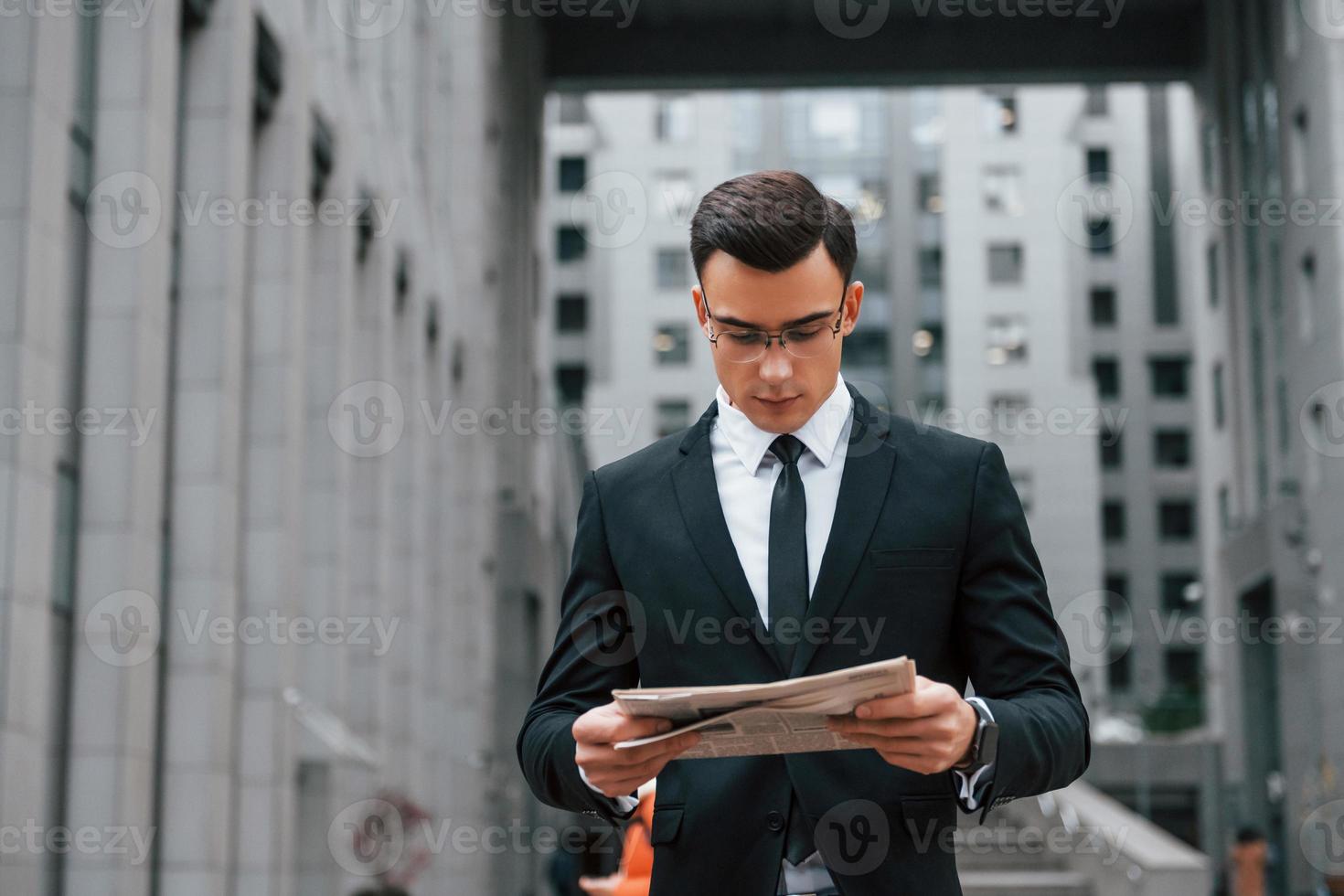 Reading some news. Businessman in black suit and tie is outdoors in the city photo