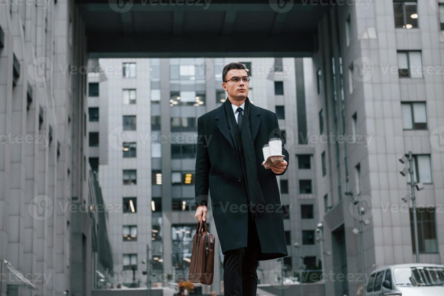 Fresh drink. Businessman in black suit and tie is outdoors in the city photo