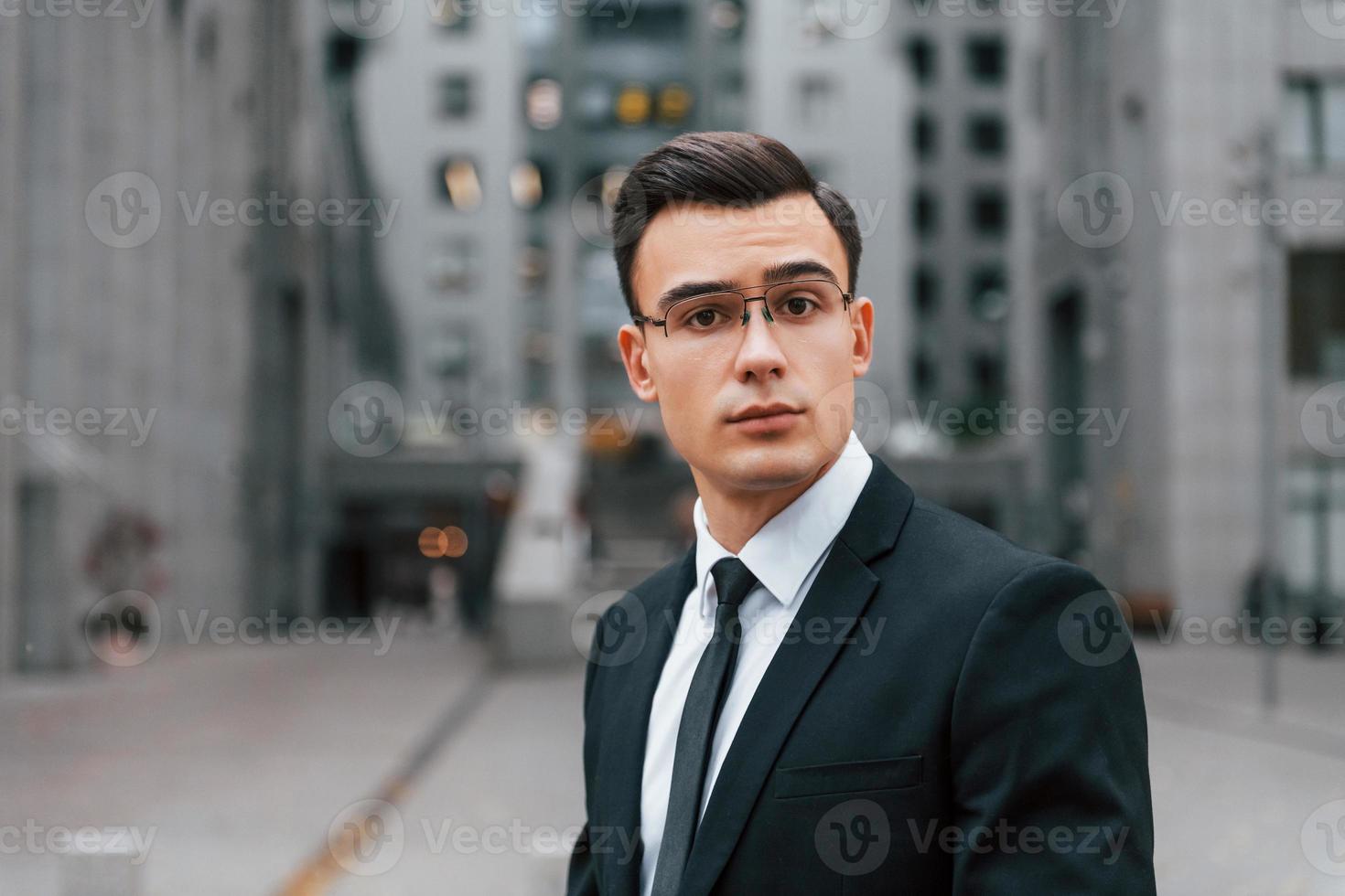 Portrait of businessman that is in black suit and tie is outdoors in the city photo