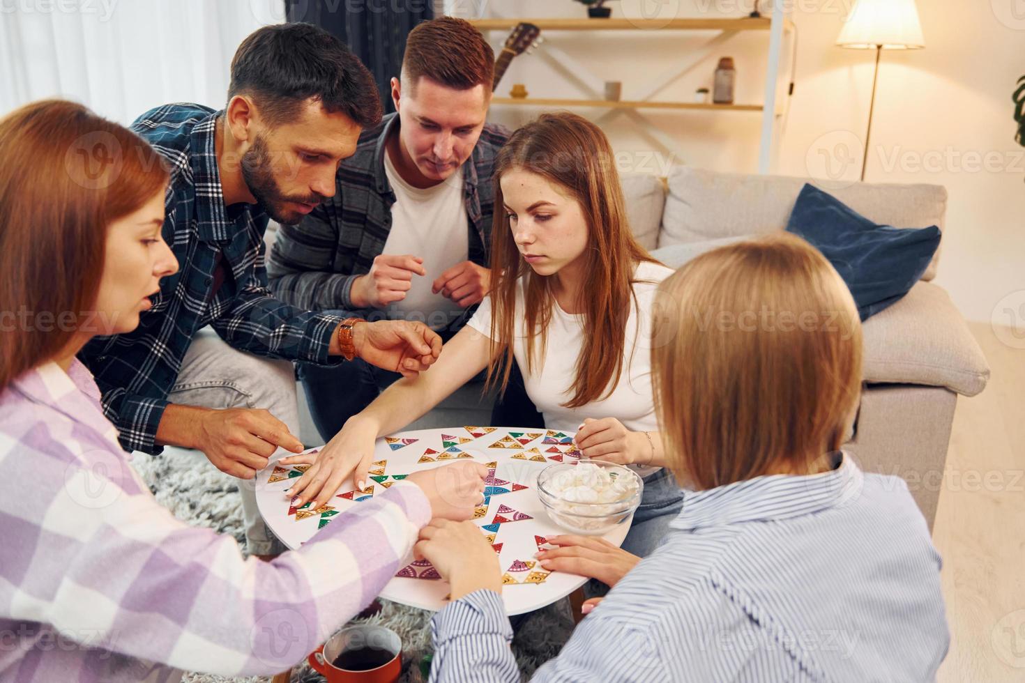 Focused at puzzle game. Group of friends have party indoors together photo
