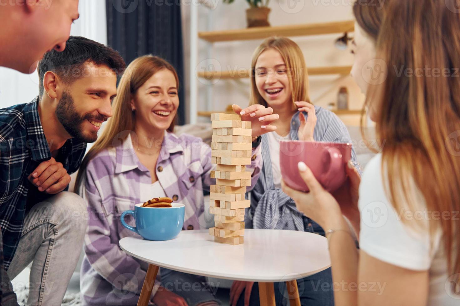 Focused on the tower building game. Group of friends have party indoors together photo