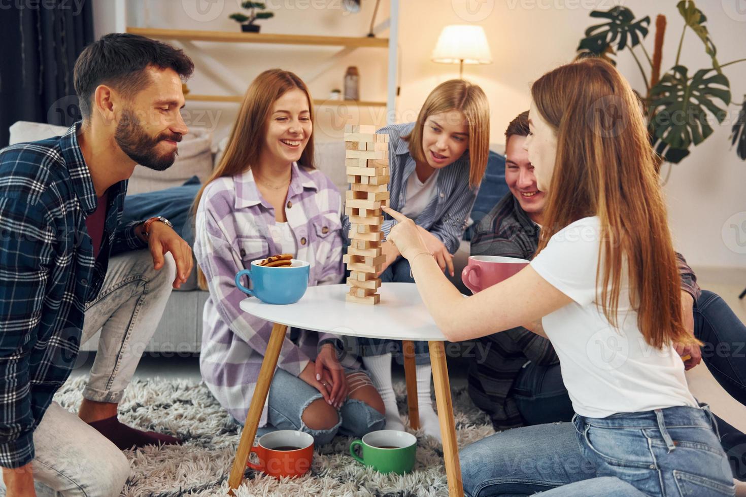 Wooden tower game on the table. Group of friends have party indoors together photo