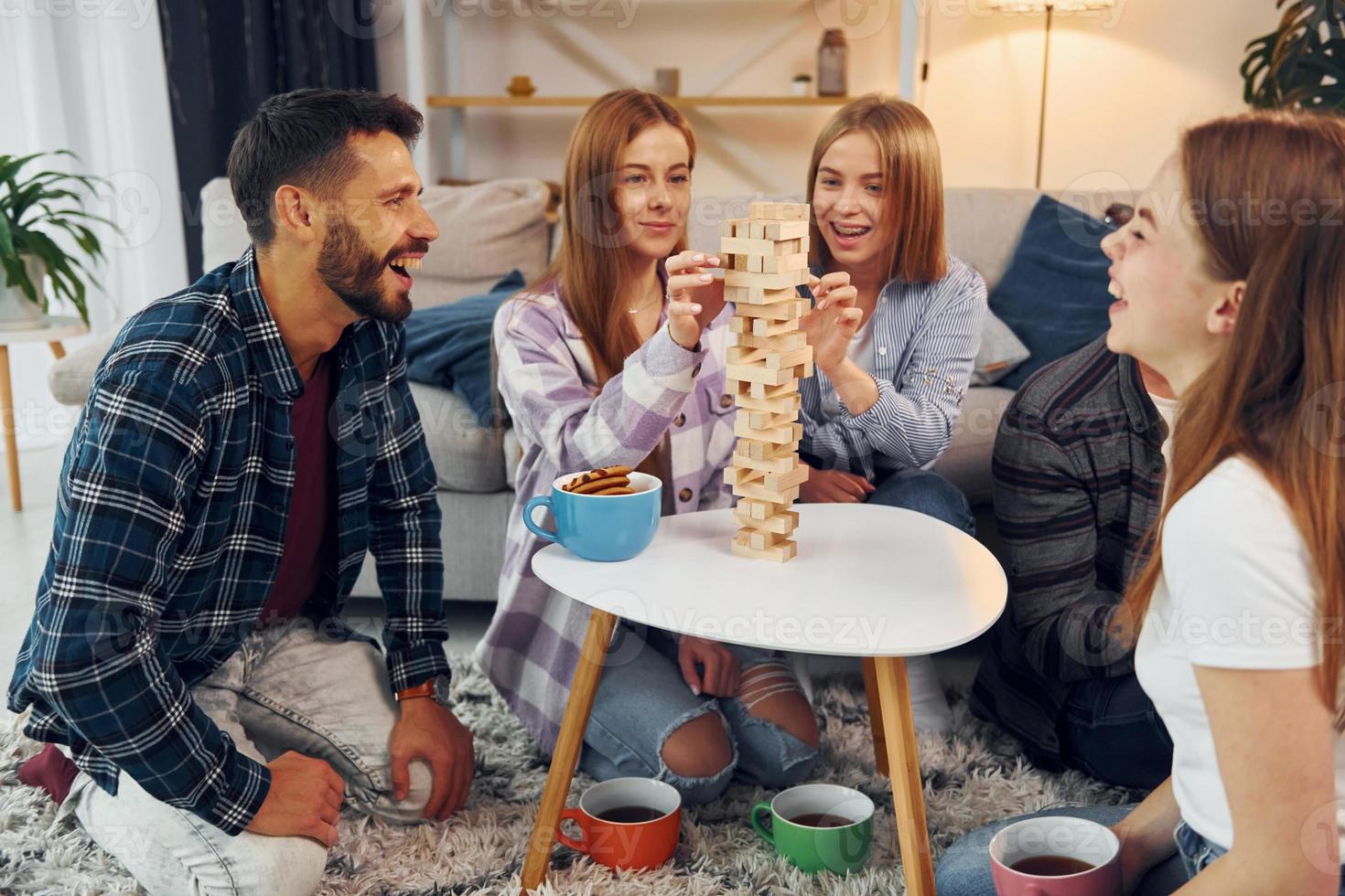 Wooden tower game on the table. Group of friends have party indoors together photo