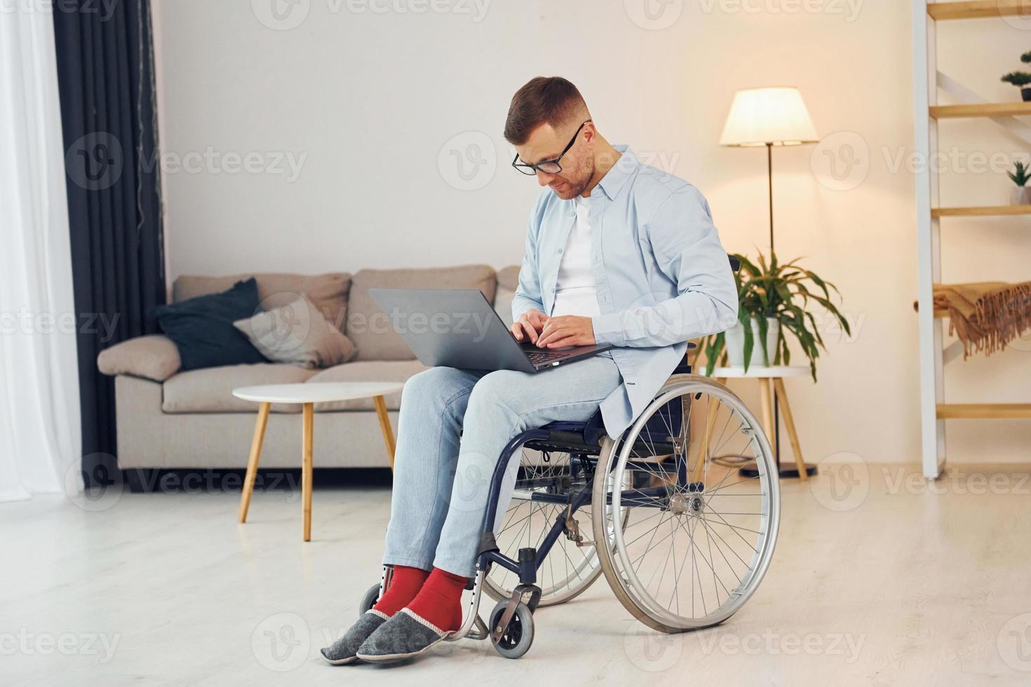 With laptop on the legs. Disabled man in wheelchair is at home photo