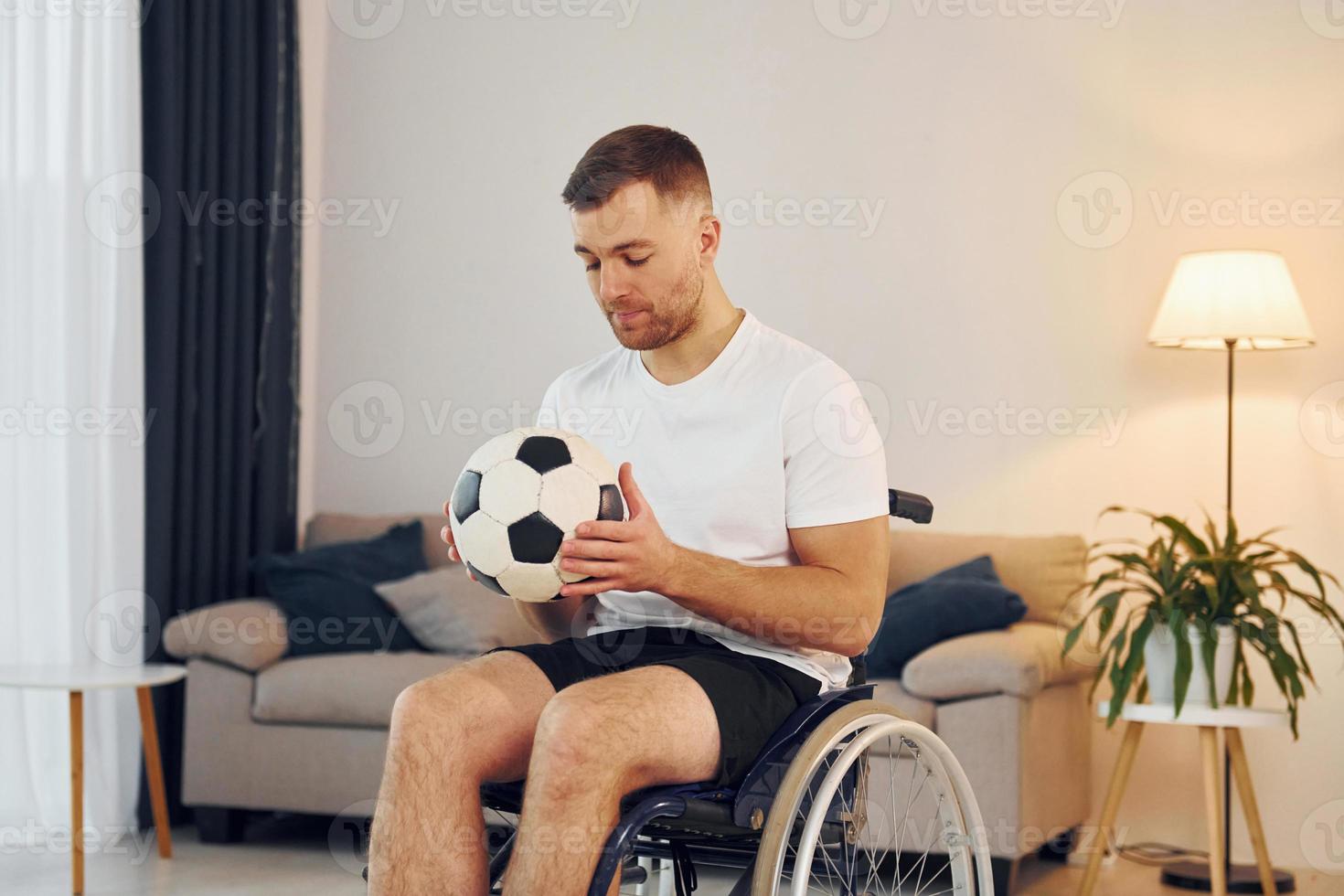 With soccer ball. Disabled man in wheelchair is at home photo