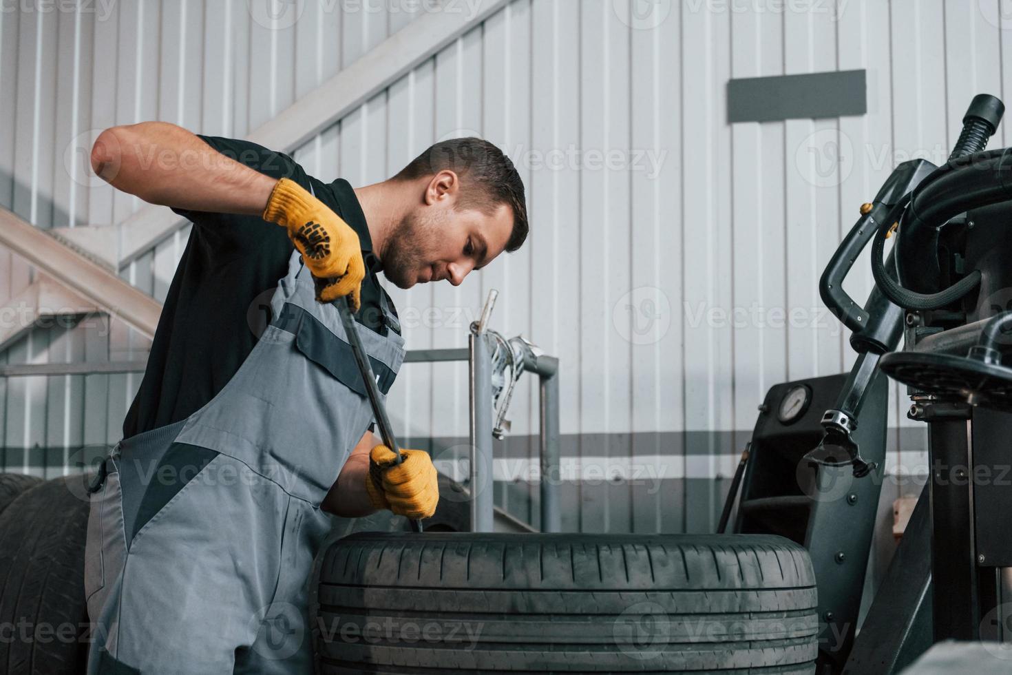 Working with broken wheel. Man in uniform is working in the auto service photo