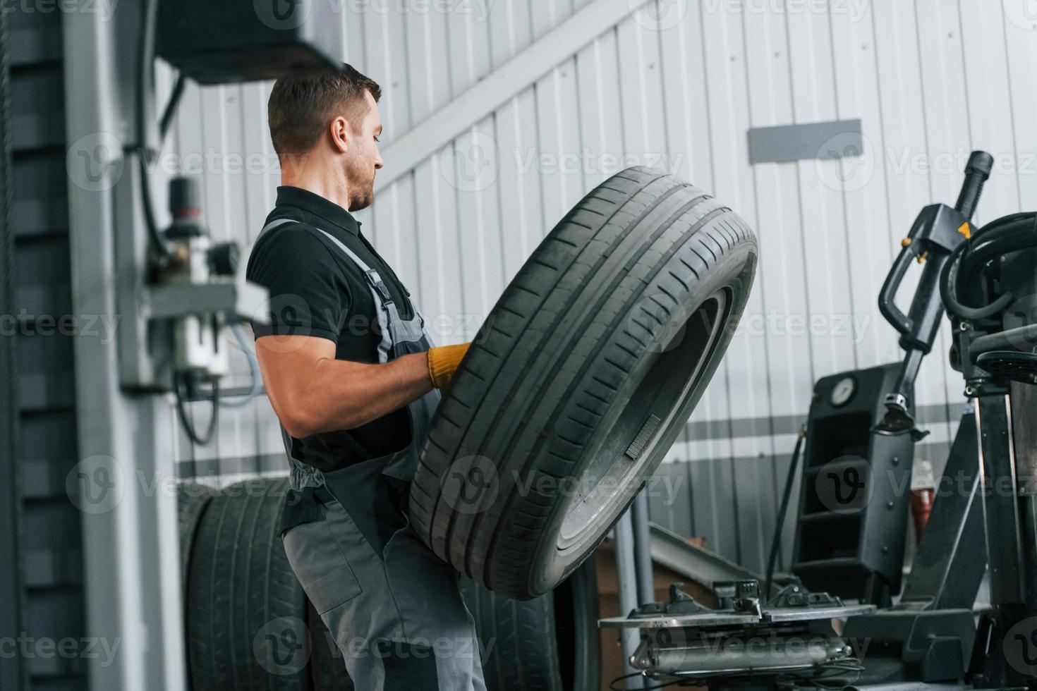 Walking and holding tyre. Man in uniform is working in the auto service photo