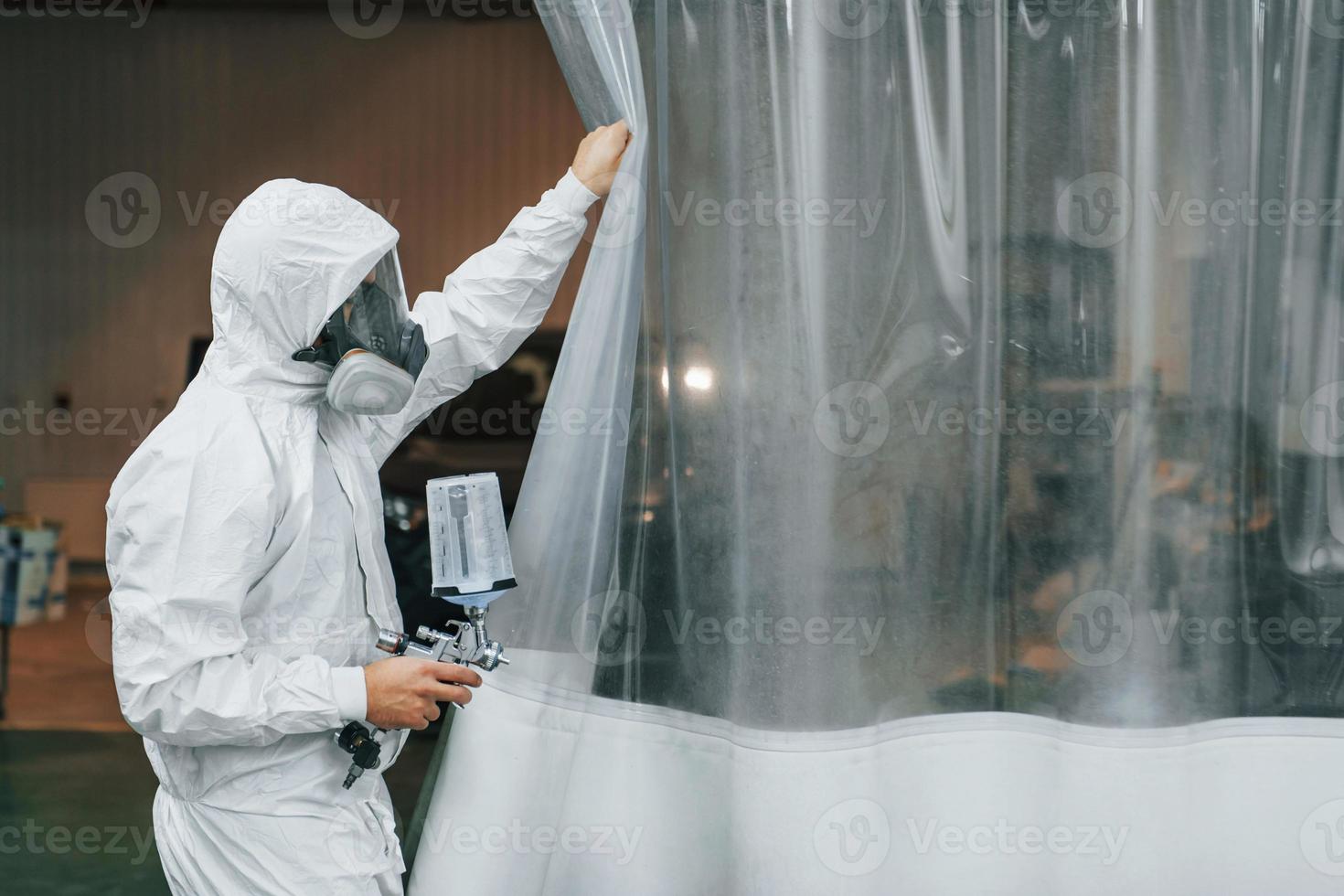 In protective white uniform. Man is working in the auto service photo