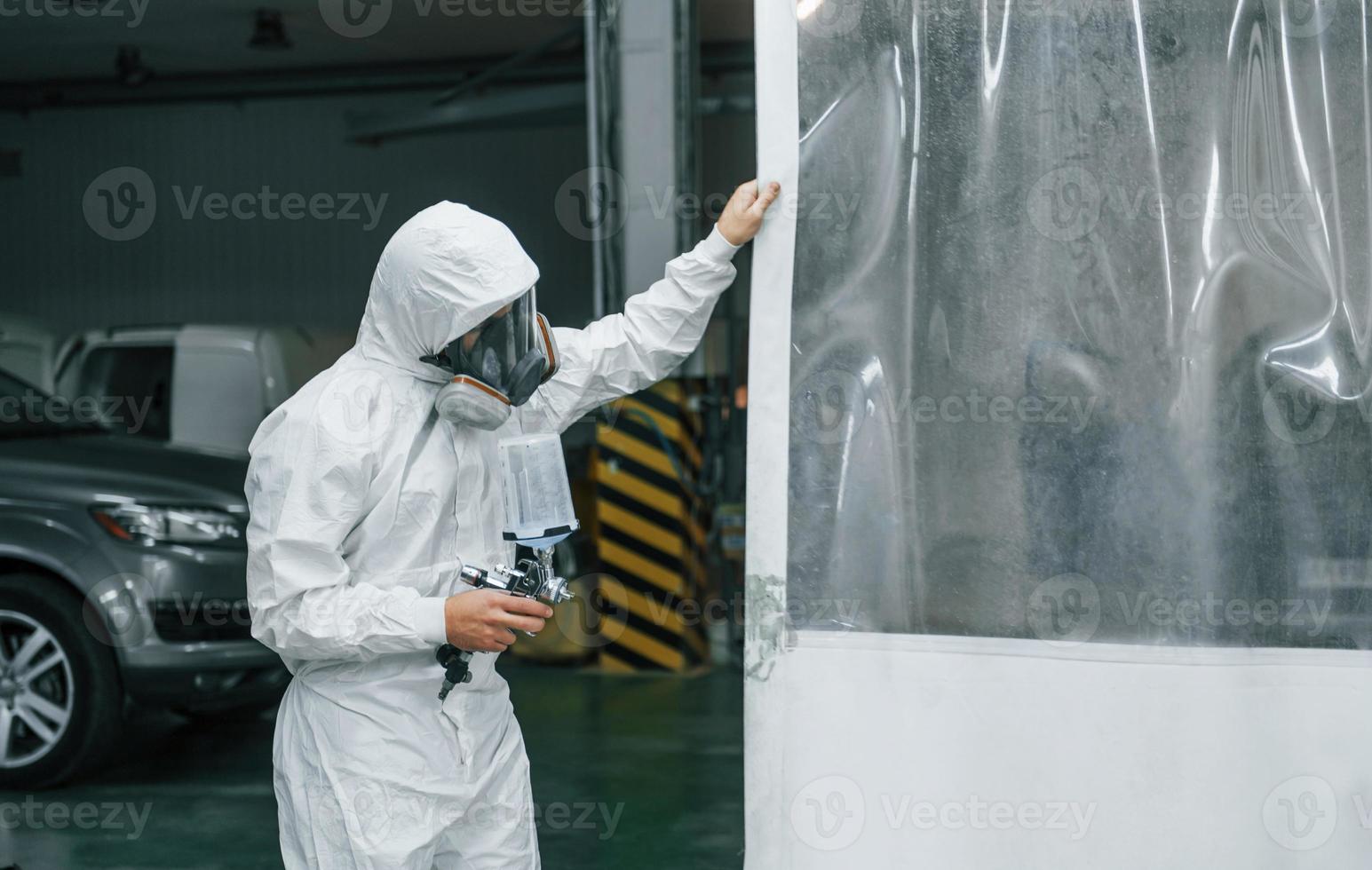 In protective white uniform. Man is working in the auto service photo