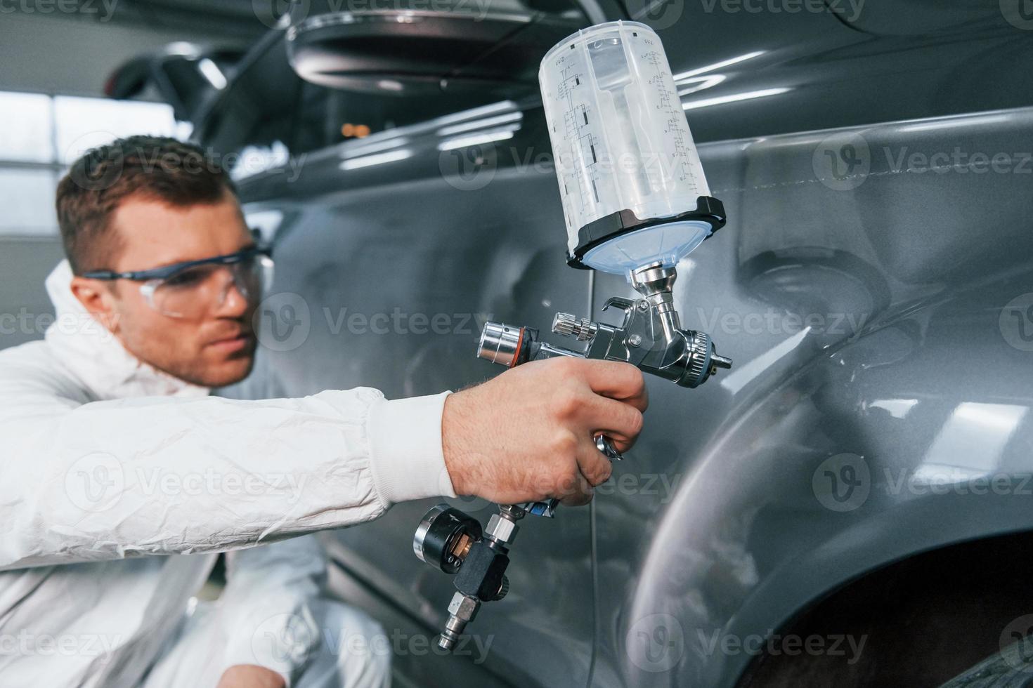 Process of painting the car. Man in uniform is working in the auto service photo