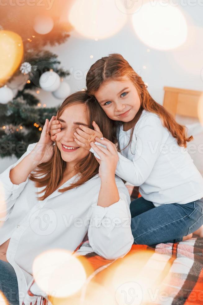 Mother with her little daughter is having fun indoors on the bed photo