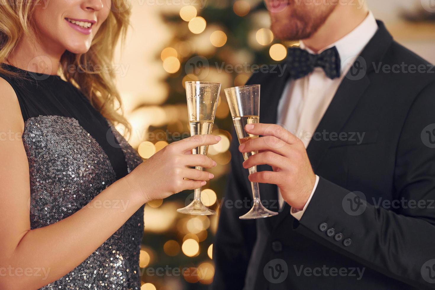 animando con vasos de alcohol. pareja feliz tiene una fiesta de año nuevo en el interior juntos foto