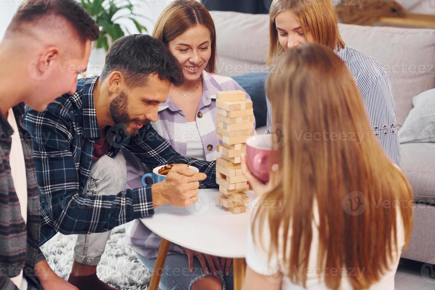 Playing wooden tower game. Group of friends have party indoors together photo