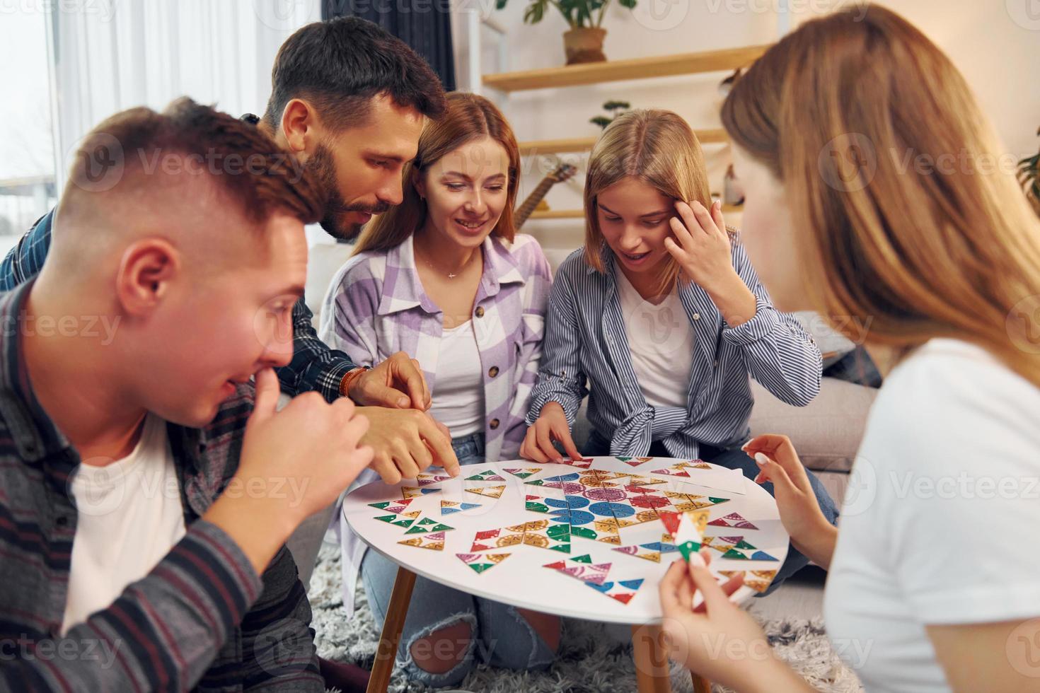 Puzzle game on the table. Group of friends have party indoors together photo
