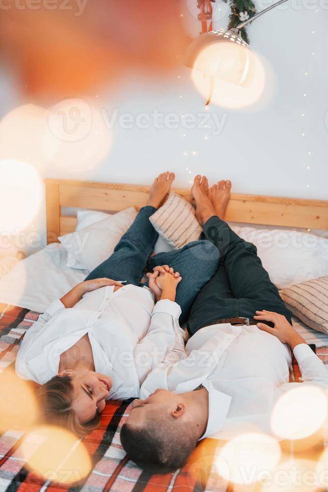 acostada en la cama. Encantadora pareja celebrando las vacaciones juntos en el interior foto