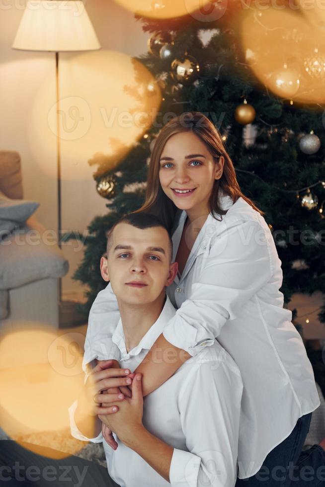 abrazándose unos a otros. Encantadora pareja celebrando las vacaciones juntos en el interior foto