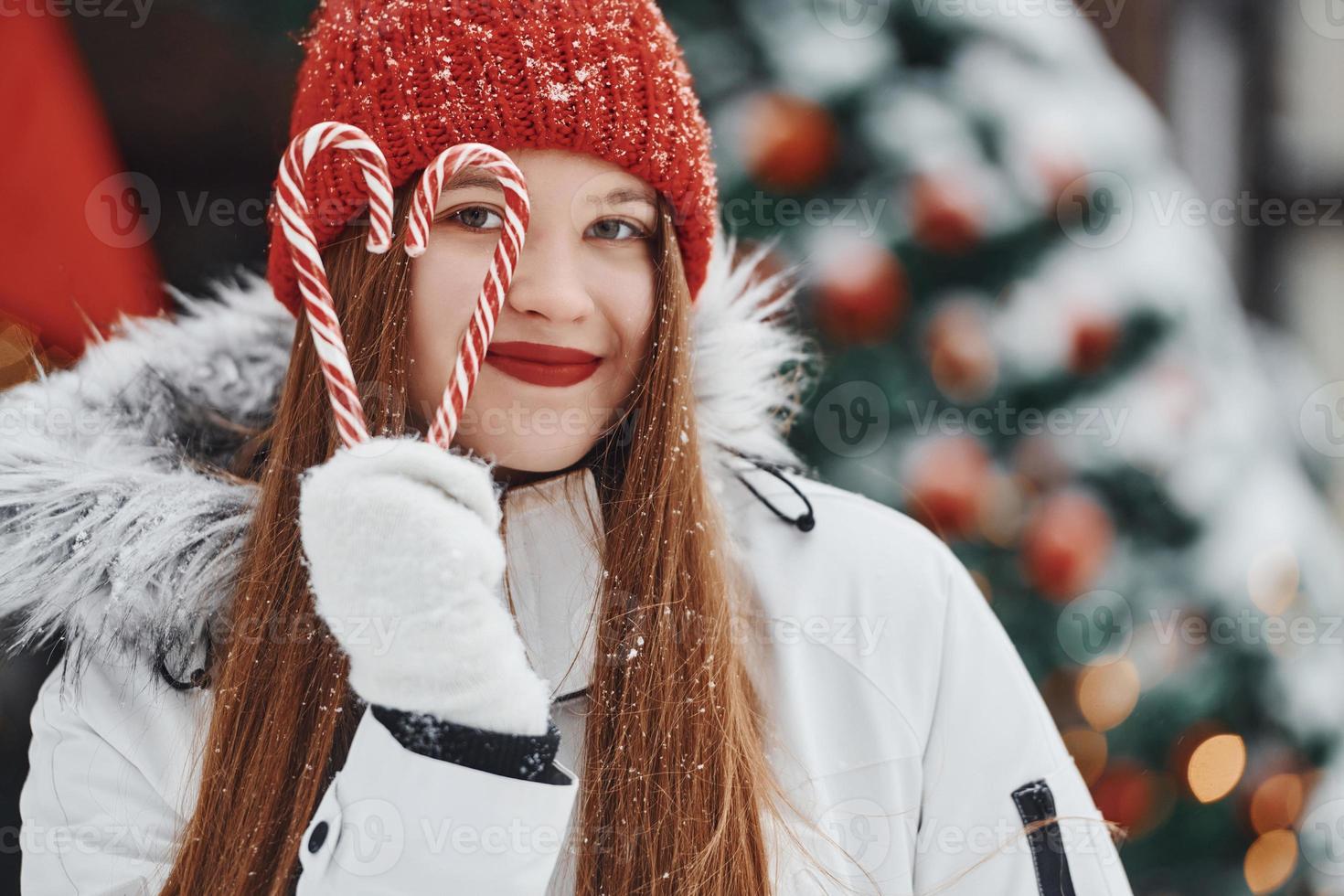 sosteniendo dulces. mujer joven feliz de pie al aire libre y celebrando las fiestas navideñas foto