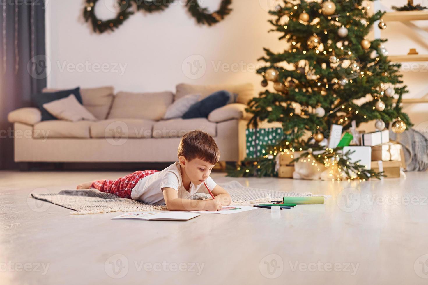 Drawing by using pencil. Little boy is in room with christmas tree is on the floor photo