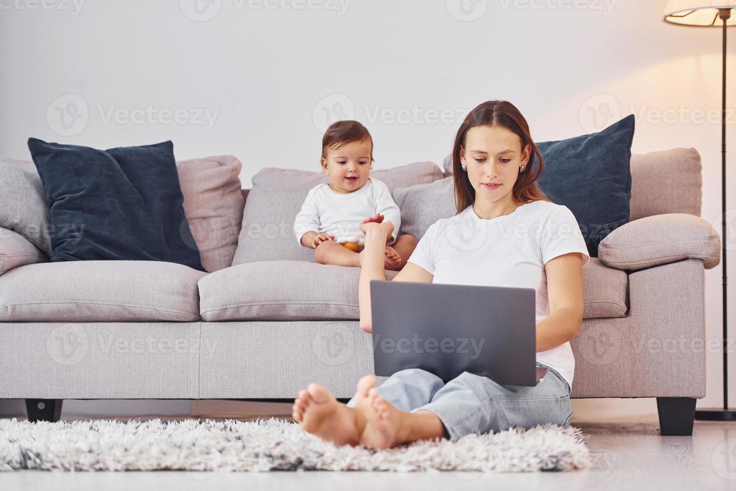 mujer trabajando usando laptop. madre con su pequeña hija está adentro en casa juntos foto