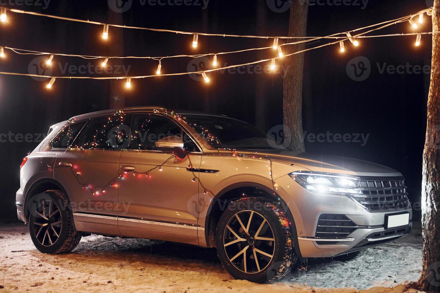 Modern silver colored automobile parked in forest with holiday decoration photo