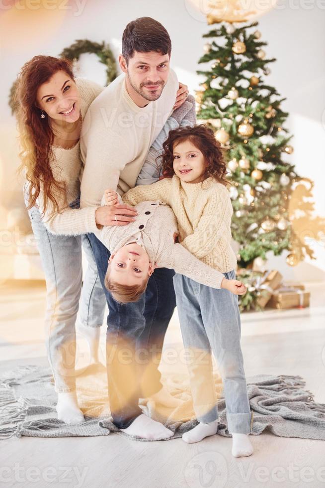 de pie en la habitación doméstica y sosteniendo al niño en las manos. familia celebrando el año nuevo con sus hijos en casa foto
