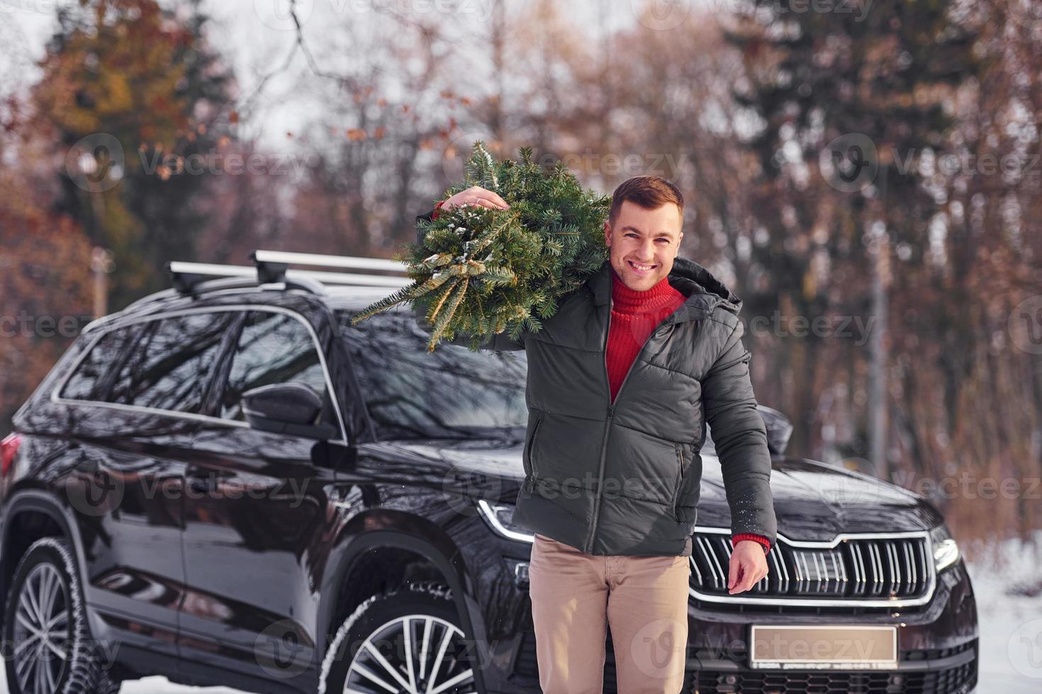 In the forest. Man with little green fir is outdoors near his car. Conception of holidays photo