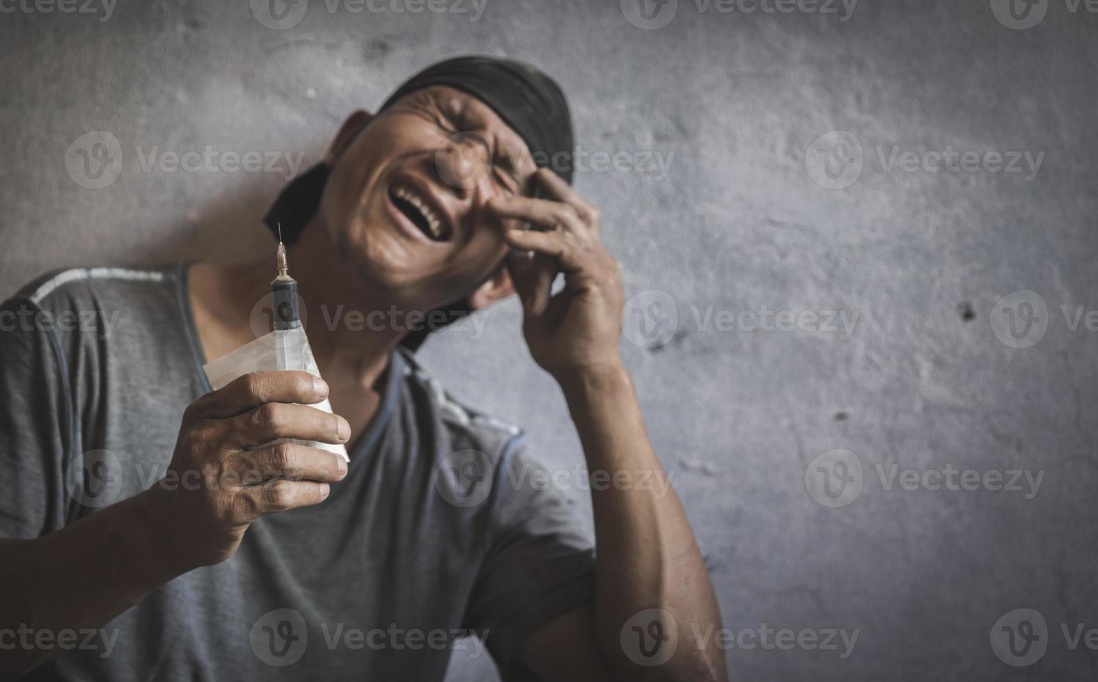 Drug addict holding a syringe about to inject intravenously.Anti-drug concept. Addicted man. Syringe.Despair.Despair.The young man is very stressed. He will be addicted to drugs. photo