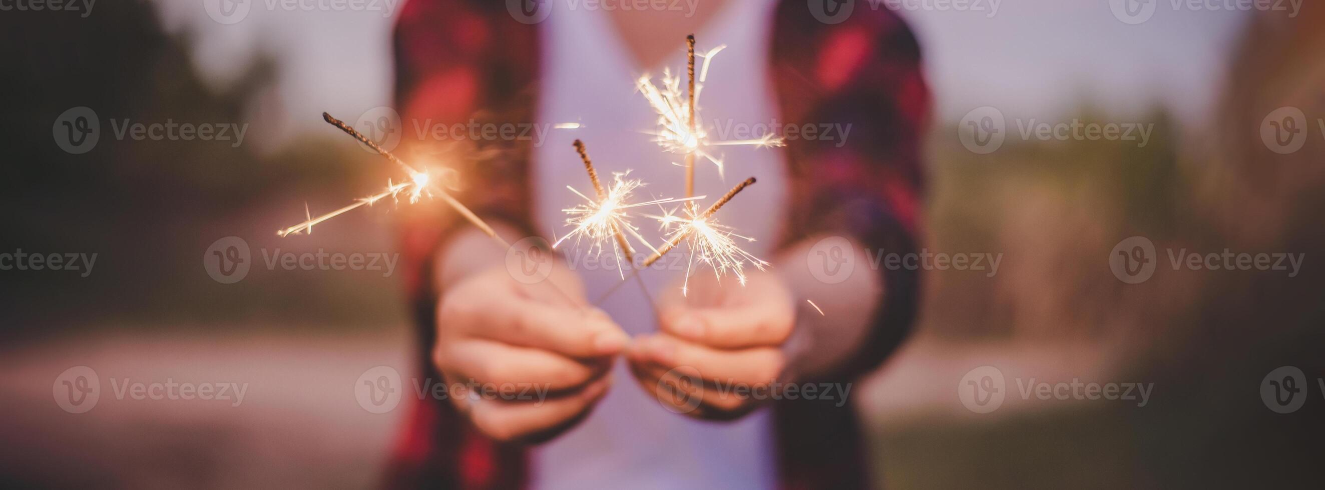 manos femeninas sosteniendo fuegos artificiales quemando bengalas jugando celebración en año nuevo foto