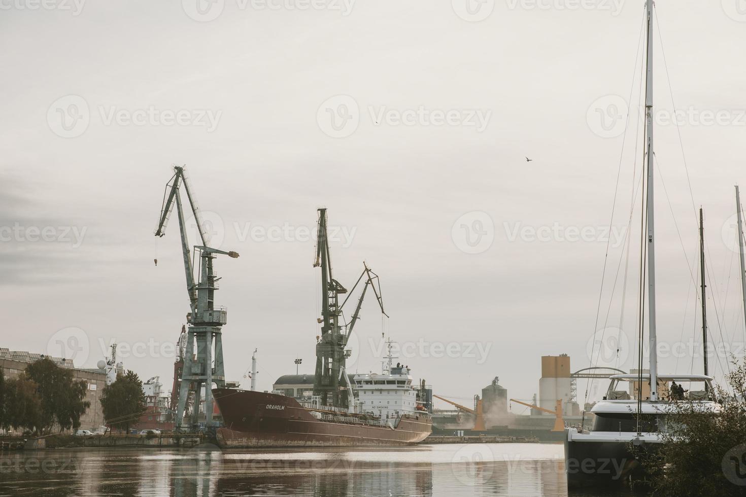 Docks on the Martwa Wisla in Poland city of Gdansk with docked cargo ship under repair and port cranes in background during cloudy autumn morning photo