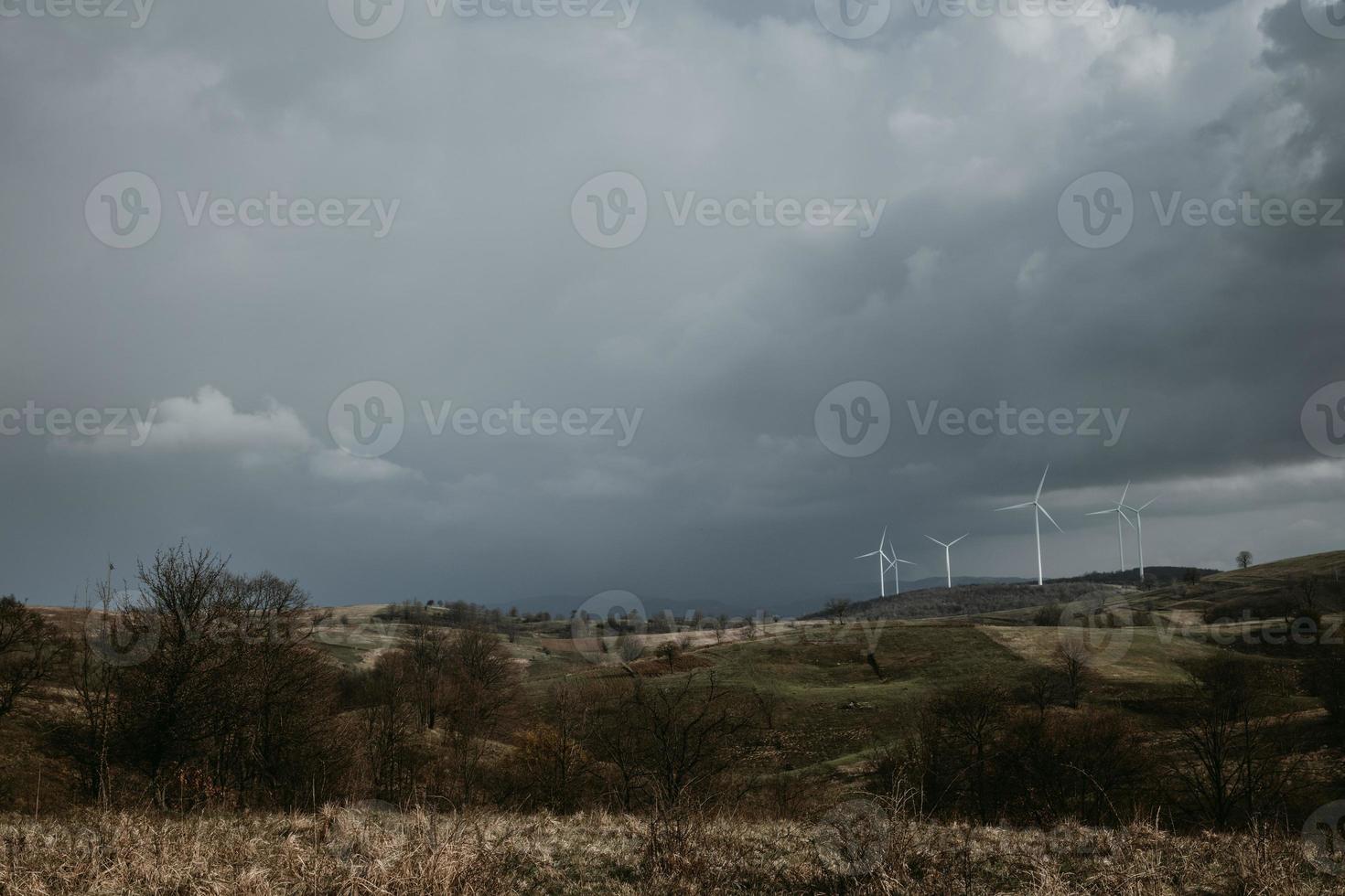 Farm of wind turbines for renewable wind energy on far horizon on hills of Romania under the dark cloudy sky. Copy space photo