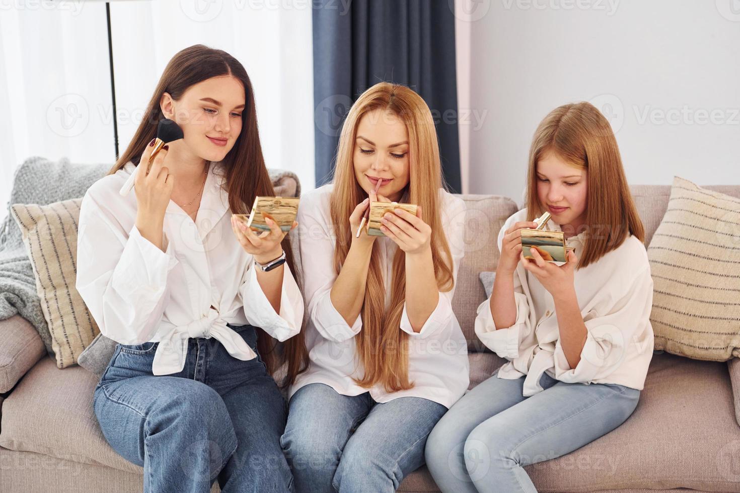 Teaching how to do make up. Young mother with her two daughters at home at daytime photo