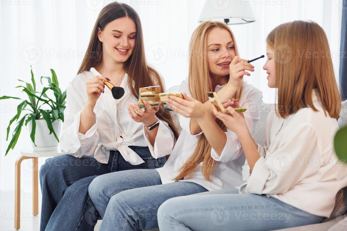 Teaching how to do make up. Young mother with her two daughters at home at daytime photo
