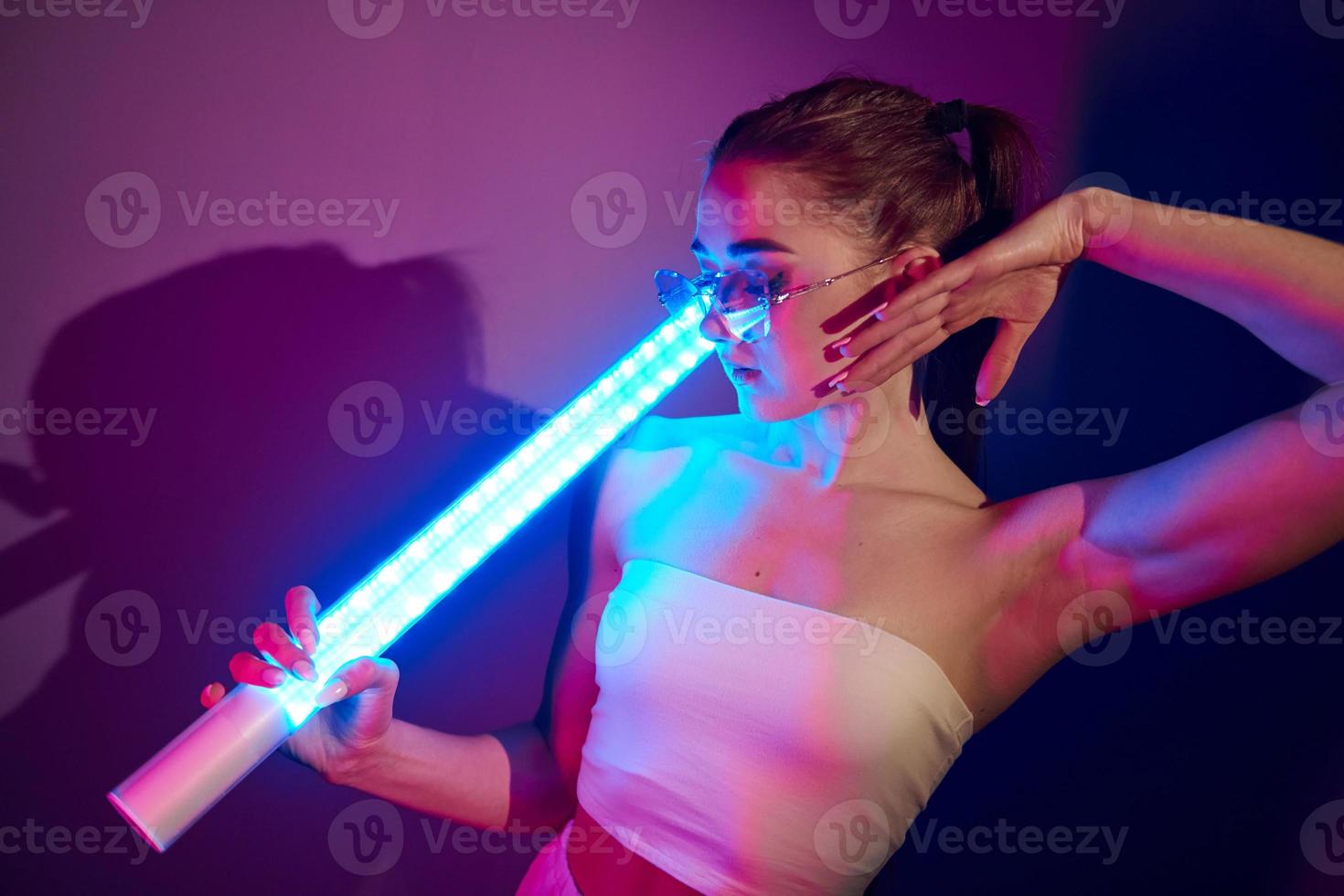 With lighting equipment. Fashionable young woman standing in the studio with neon photo