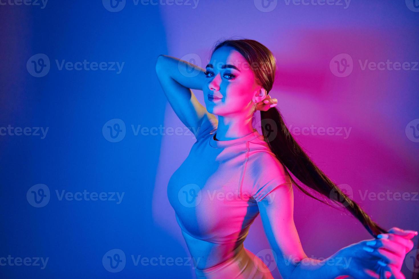 Long brown colored hair. Fashionable young woman standing in the studio with neon light photo