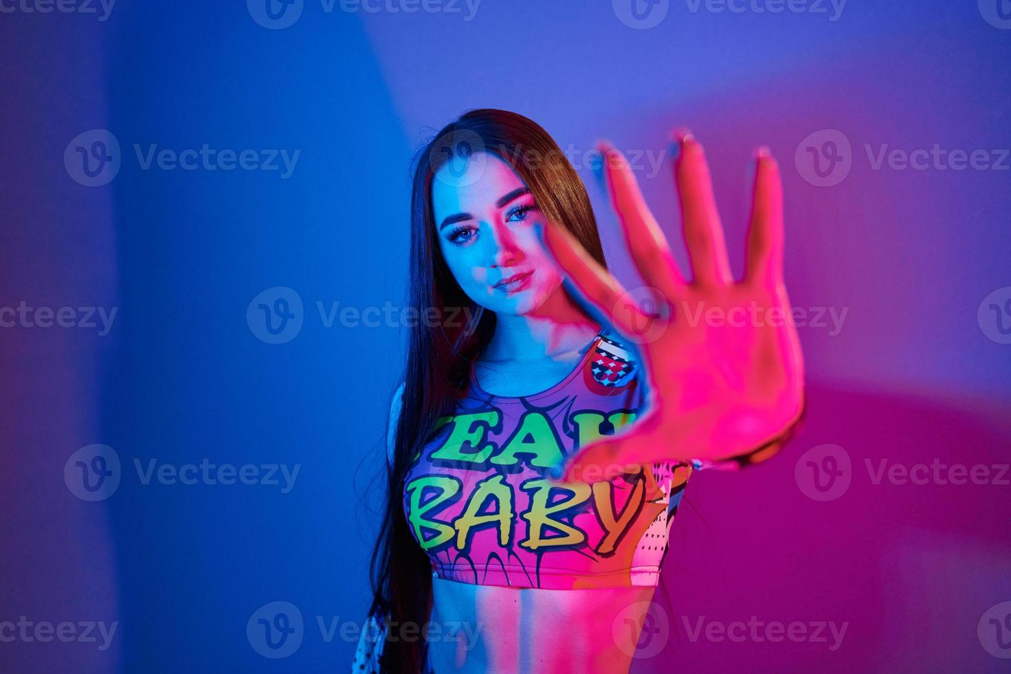 parada, gesto. joven de moda parada en el estudio con luz de neón foto