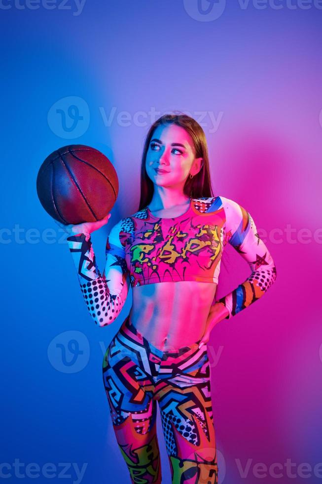 In colorful clothes. Fashionable young woman standing in the studio with neon light photo
