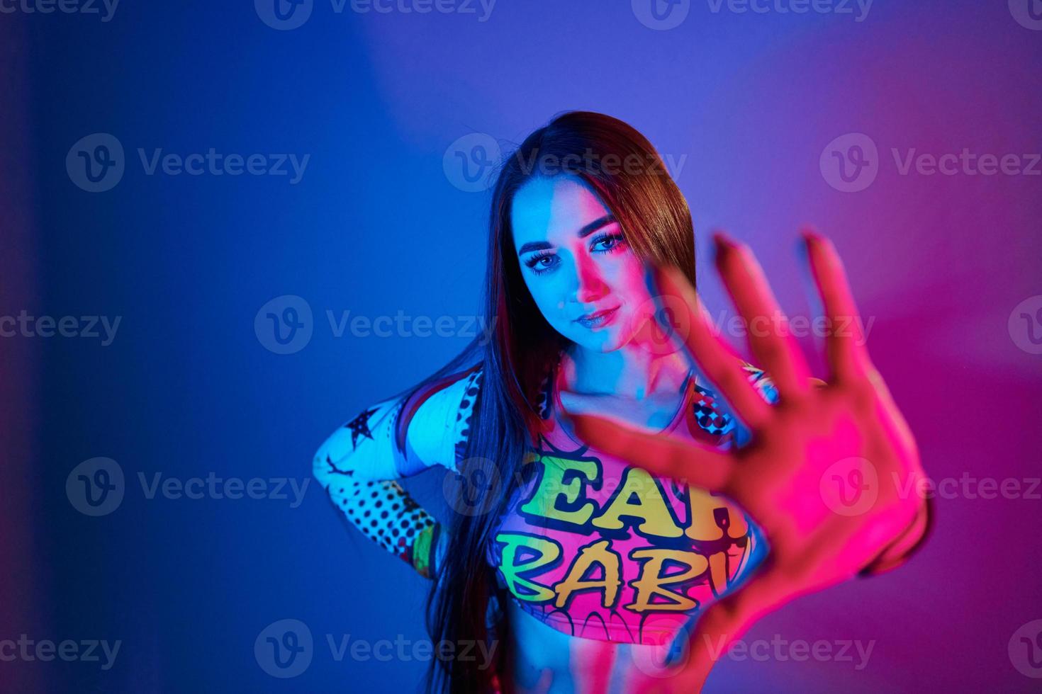 Stop, gesture. Fashionable young woman standing in the studio with neon light photo