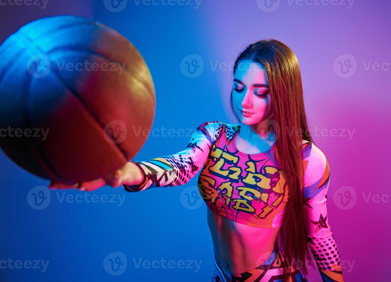 In colorful clothes. Fashionable young woman standing in the studio with neon light photo