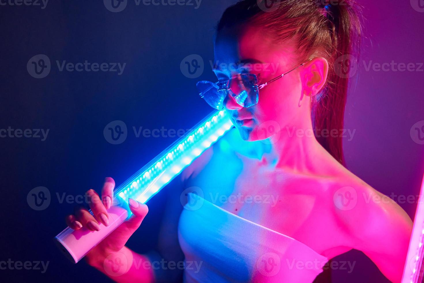 With lighting equipment. Fashionable young woman standing in the studio with neon photo