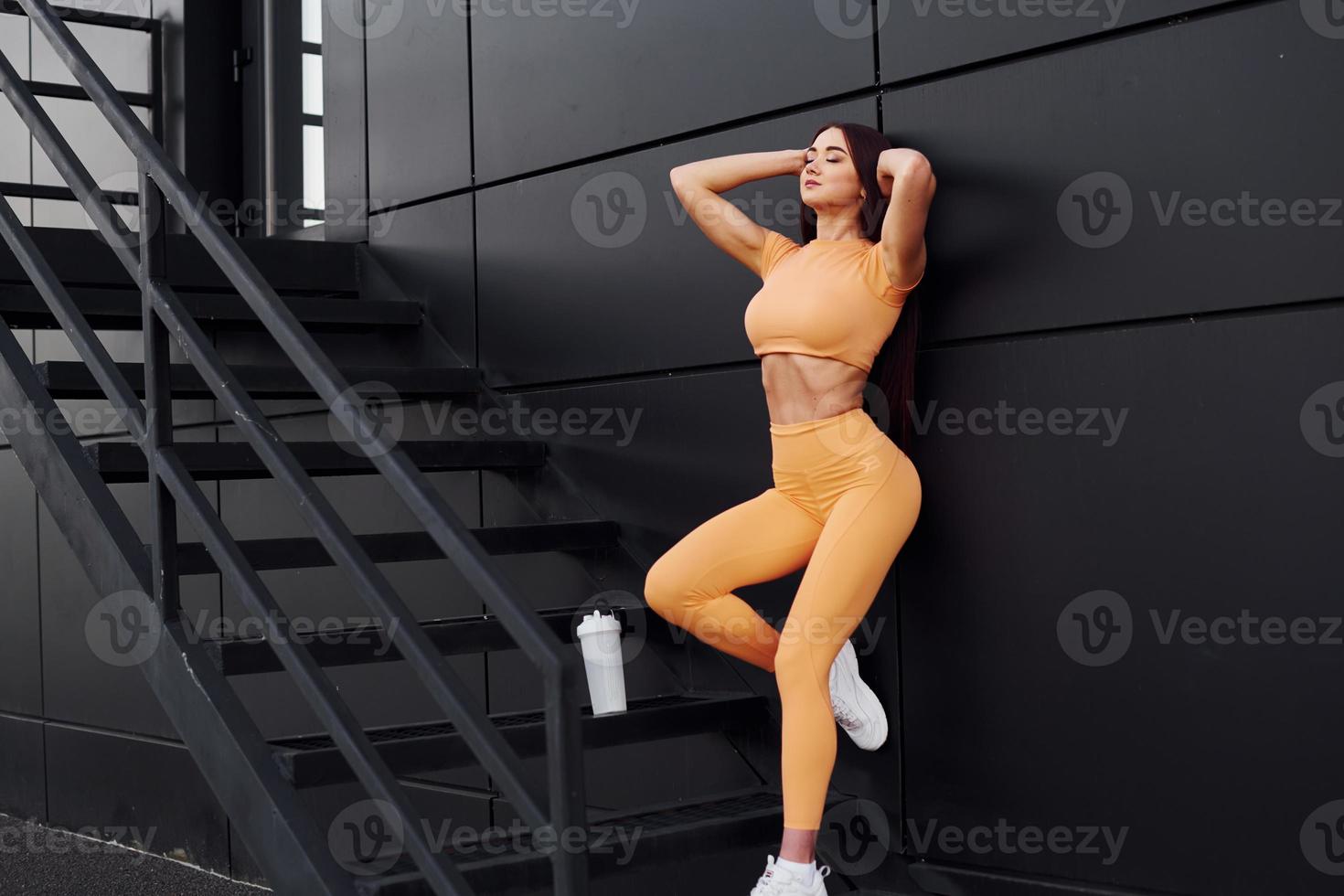 On stairs with bottle of water. Young woman in sportswear have fitness session outdoors photo