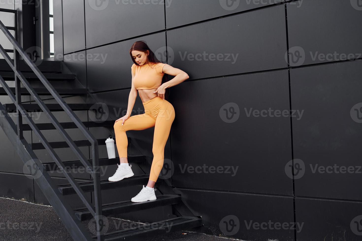 On stairs with bottle of water. Young woman in sportswear have fitness session outdoors photo