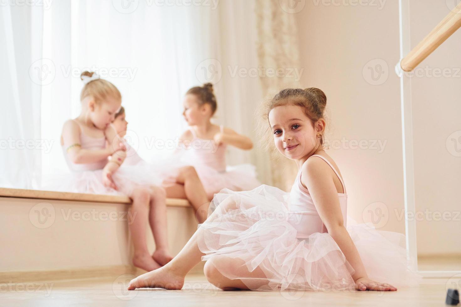 Girl sits on the floor. Little ballerinas preparing for performance by practicing dance moves photo
