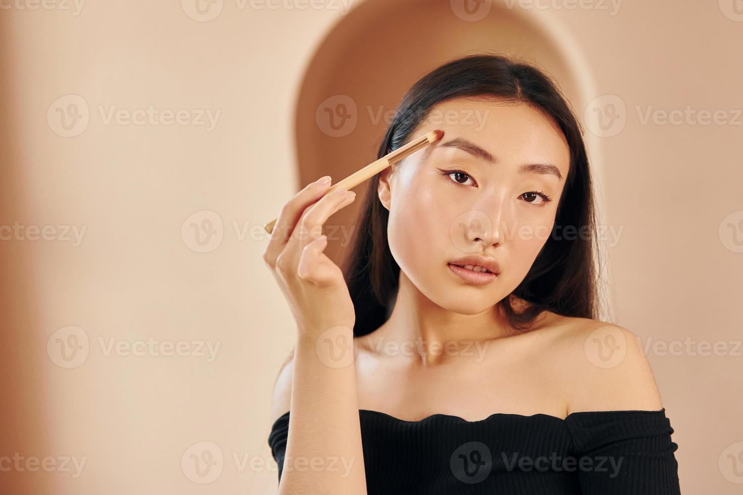 Make up brush. Young serious asian woman standing indoors photo