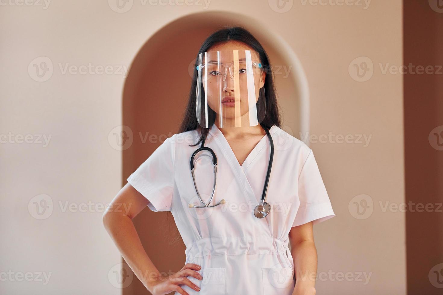In protective wear. Young serious asian woman standing indoors photo