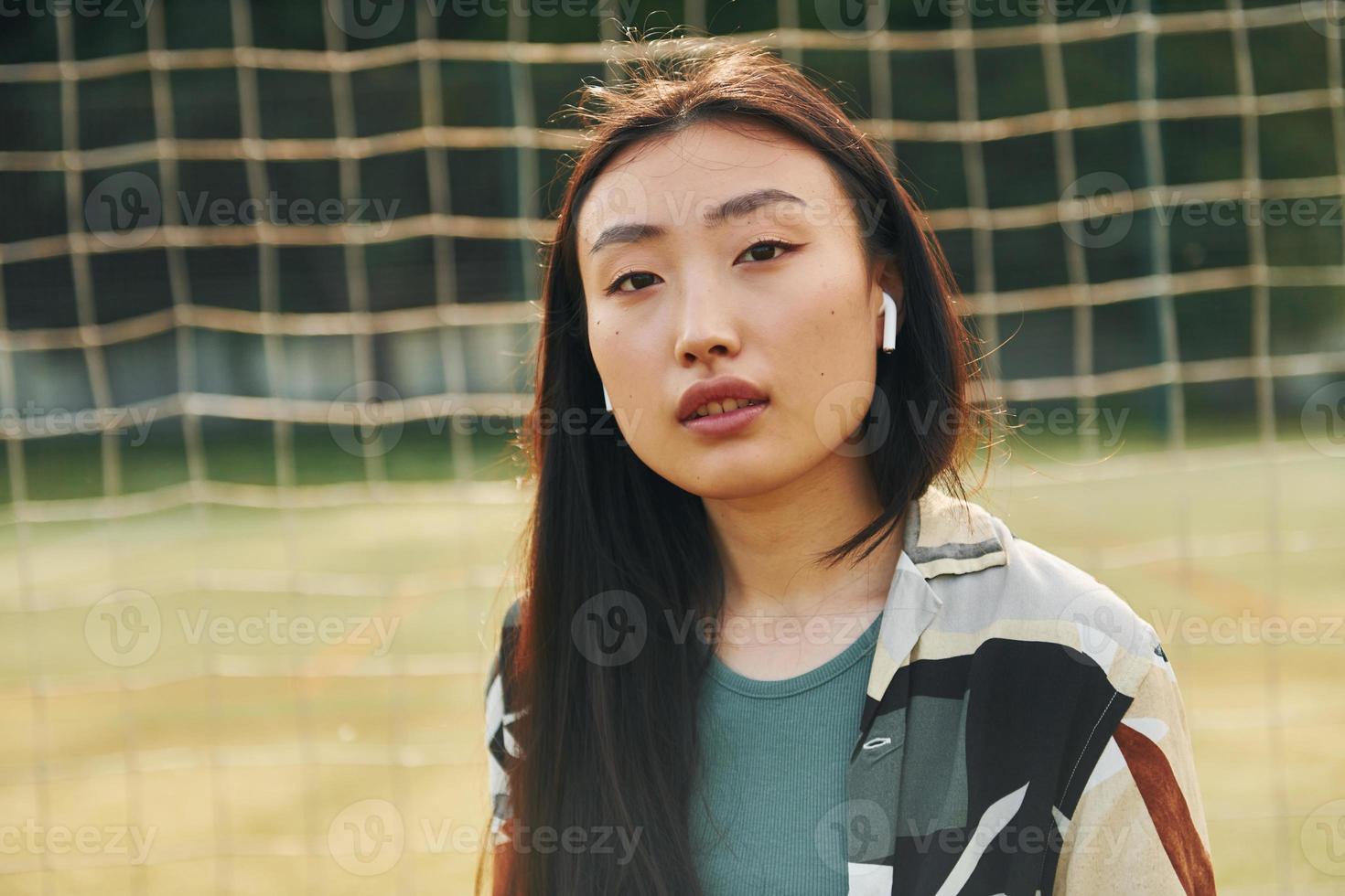 Against net of sport field. Young asian woman is outdoors at daytime photo